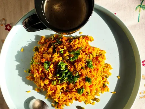 A plate of vegetable poha garnished with coriander and lemon